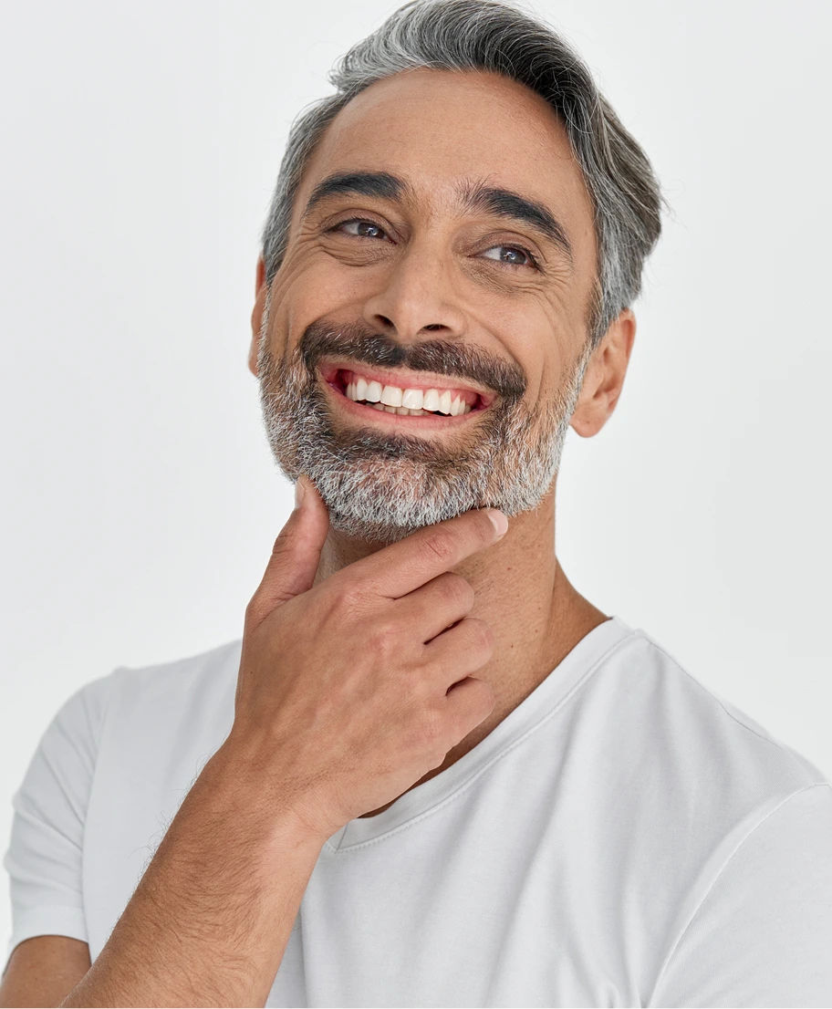 Man with gray beard smiling and touching his chin, displaying white teeth