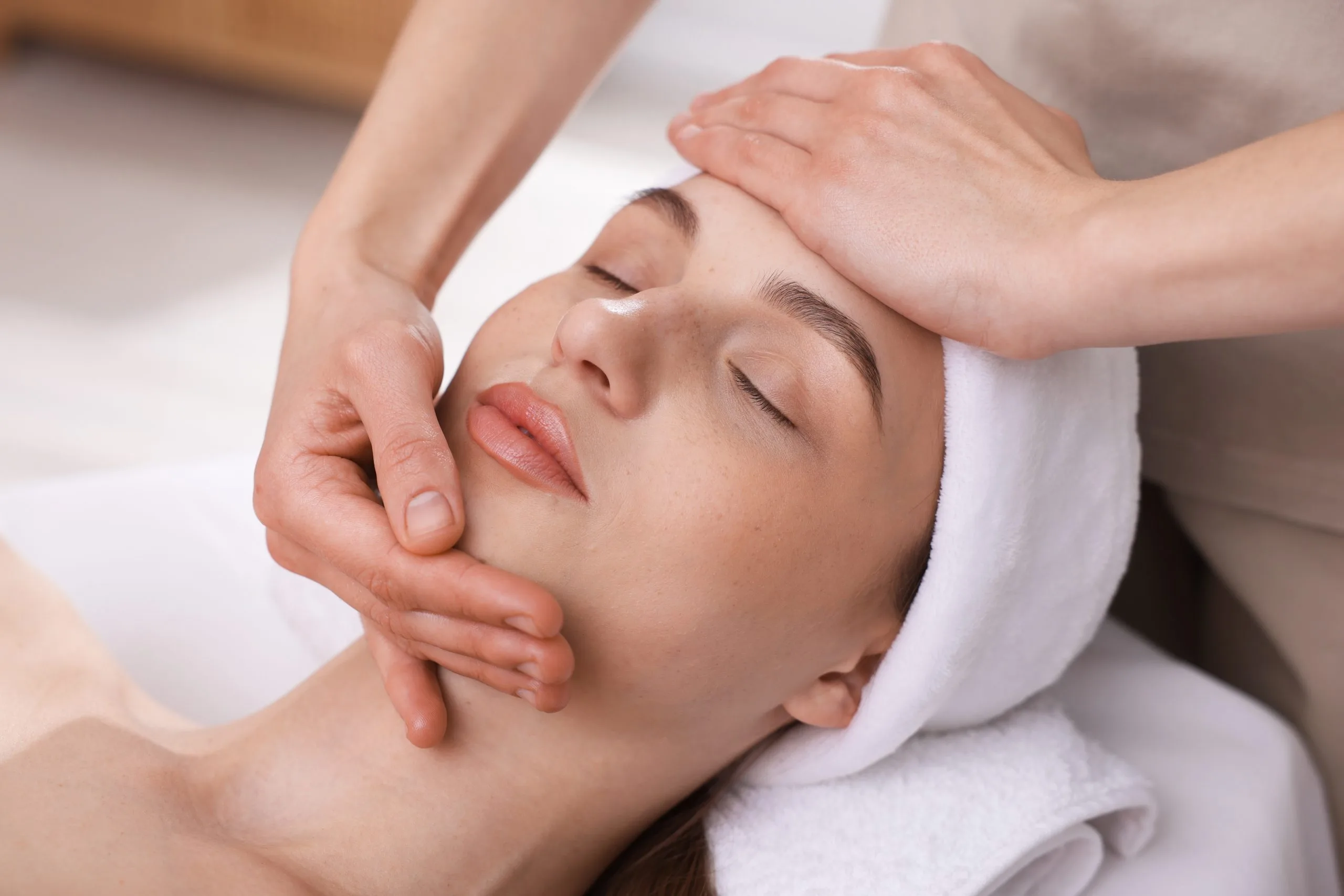 Esthetician giving facial massage to relaxed patient wearing white headband