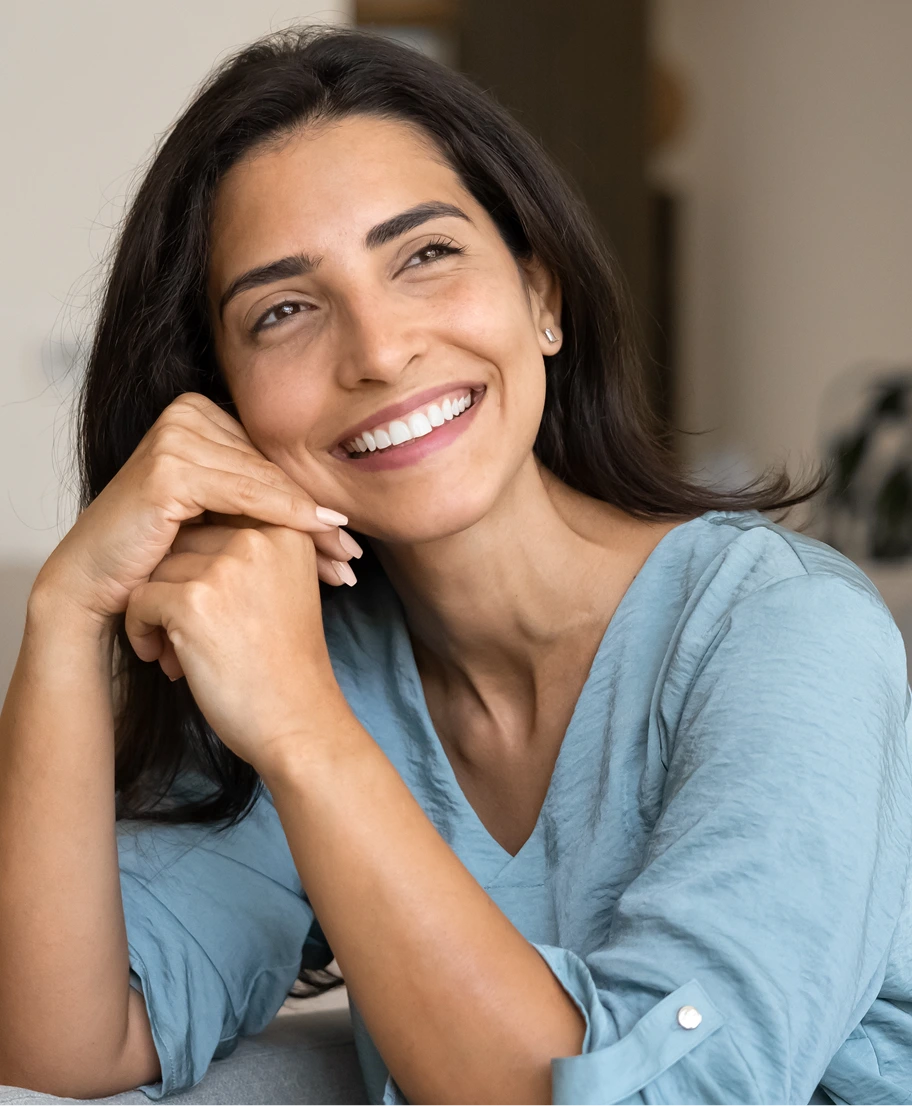 Woman with long dark hair smiling with hand near face, wearing light blue shirt