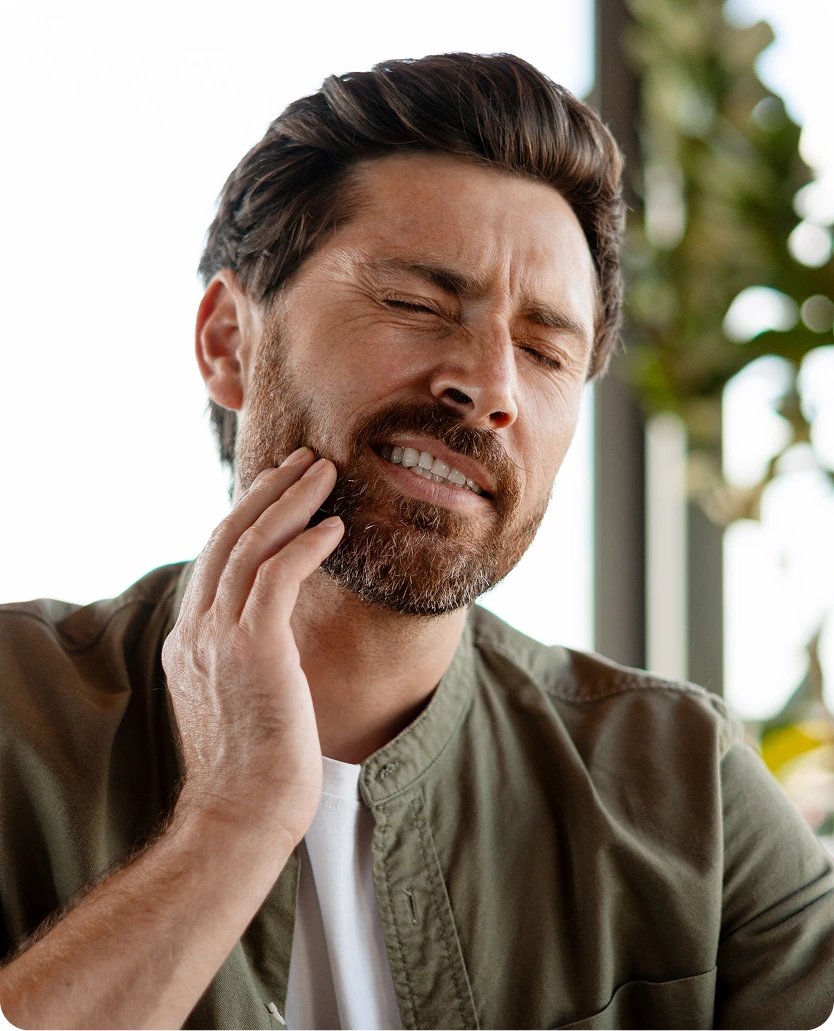 Man with hand on jaw, grimacing from TMJ pain