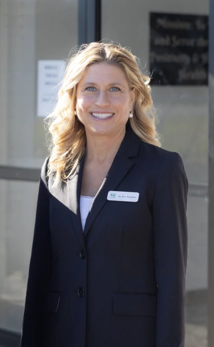 Woman in black blazer standing outside Divine Dental office with lotus and tooth logo on white brick wall