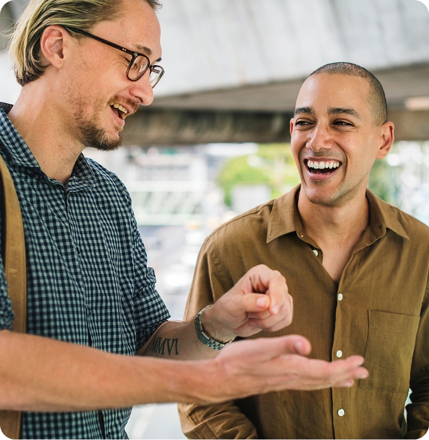 Two men laughing together while conversing outdoors near building