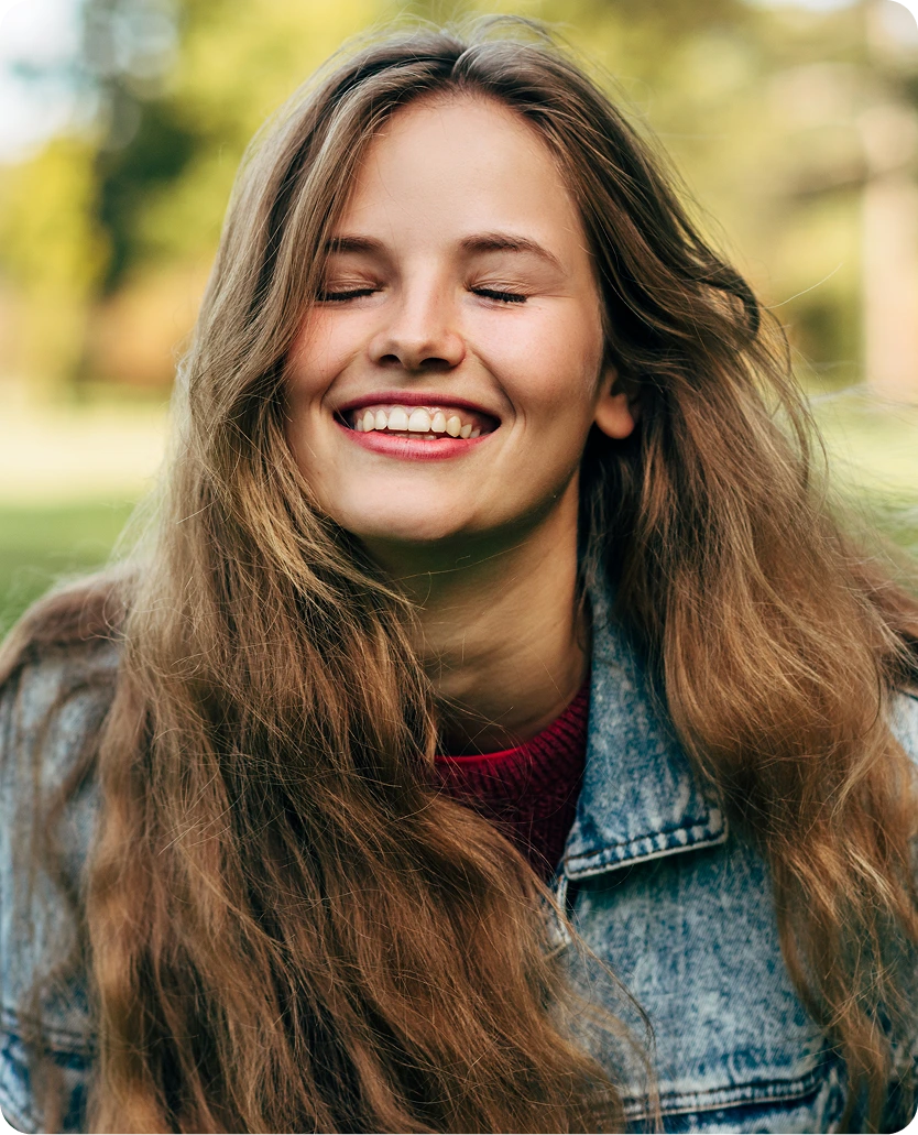 Woman smiling outdoors with long brown hair wearing a denim jacket