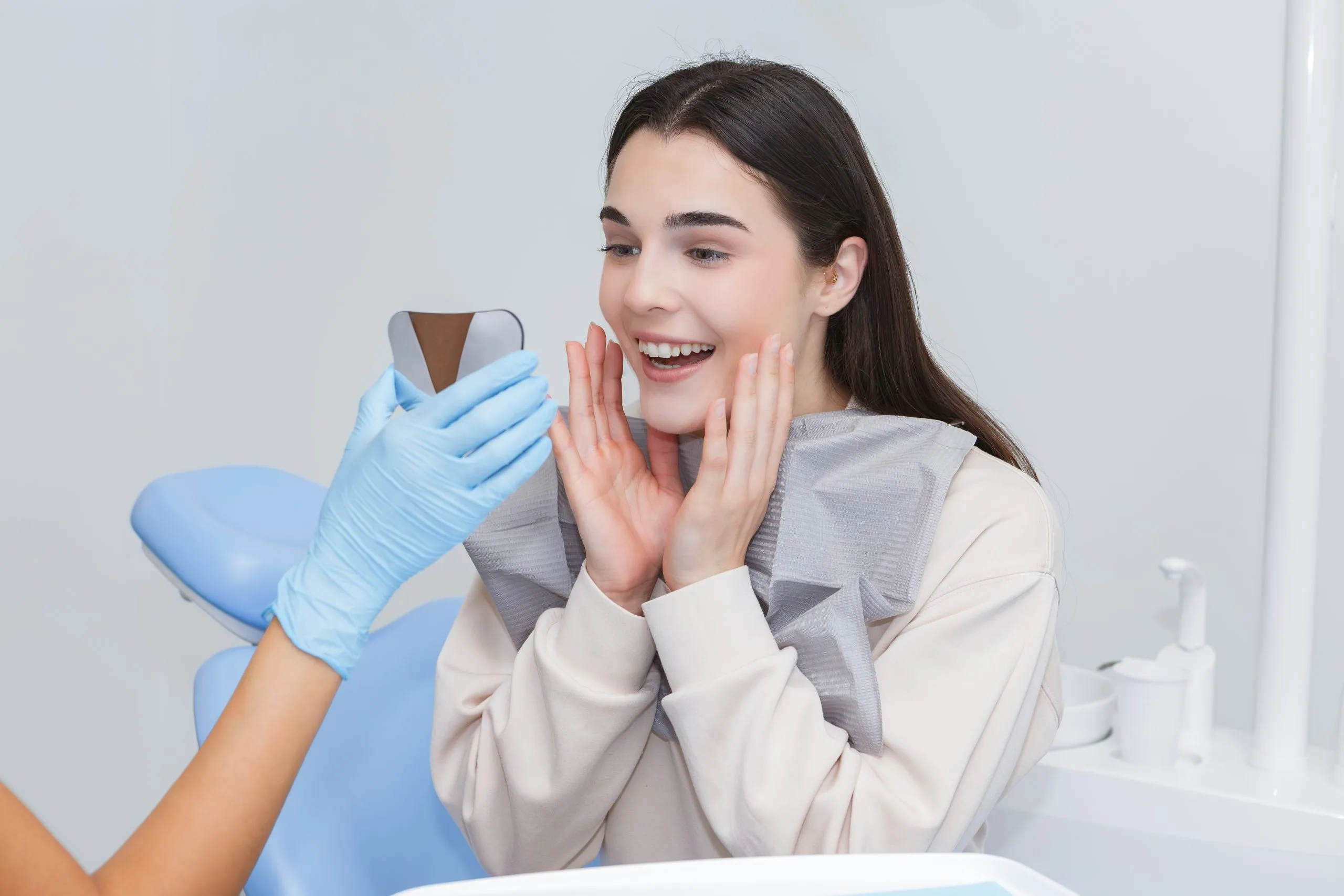Smiling woman in dental chair reacting positively as dentist in blue gloves shows her a dental scan