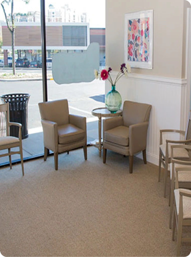 Maryland Holistic Dentistry waiting room with two tan armchairs, side table with flowers, colorful artwork, and street view windows