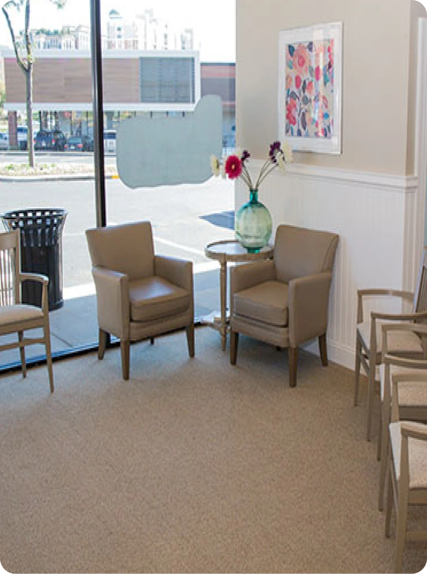 Maryland Holistic Dentistry waiting room with two tan armchairs, side table with flowers, colorful artwork, and street view windows