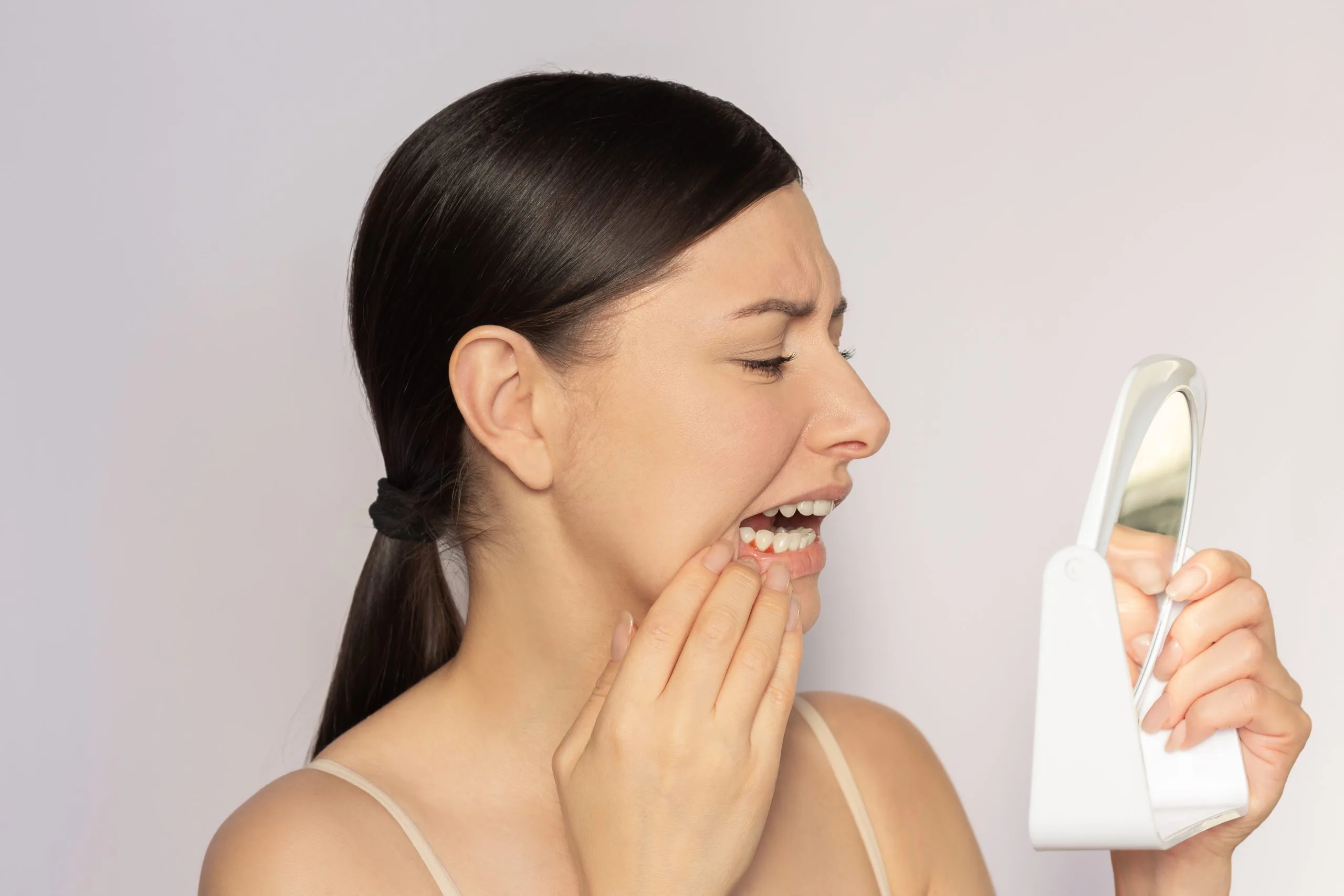 Woman touching her cheek and examining her teeth in a handheld mirror